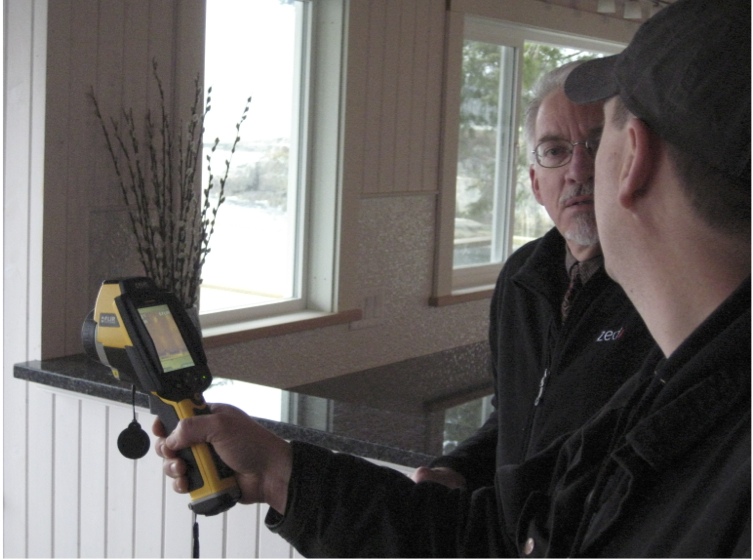 Thermal imaging expert conducting real-time assessment of heat loss with hand-held infrared camera. The householder is actively engaged and immediately understands the heat lost with the images provides.  Photo Credit: Stephen Sheppard